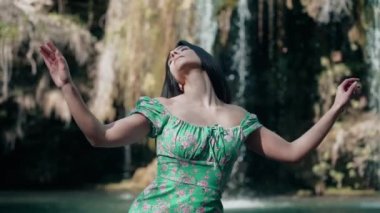 Bir dağ şelalesinin yanında poz veren turkuaz elbiseli güzel bir manken. Vahşi yaşam kavramı.