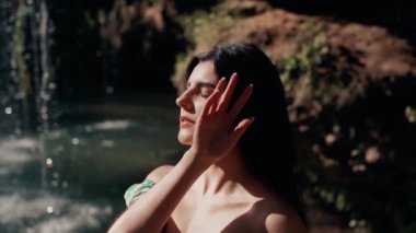 Bir dağ şelalesinin yanında poz veren turkuaz elbiseli güzel bir manken. Vahşi yaşam kavramı.