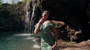Bir dağ şelalesinin yanında poz veren turkuaz elbiseli güzel bir manken. Vahşi yaşam kavramı.