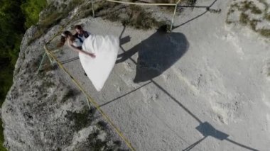 Deniz kıyısındaki bir uçurumun kenarında düğün. Gelin ve damat yüksek uçurumun kenarında duruyorlar. Günbatımı ışığının 4k hava aracı videosu
