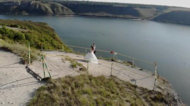 Deniz kıyısındaki bir uçurumun kenarında düğün. Gelin ve damat yüksek uçurumun kenarında duruyorlar. Günbatımı ışığının 4k hava aracı videosu