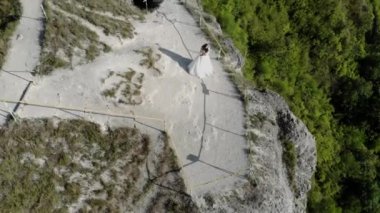 Deniz kıyısındaki bir uçurumun kenarında düğün. Gelin ve damat yüksek uçurumun kenarında duruyorlar. Günbatımı ışığının 4k hava aracı videosu