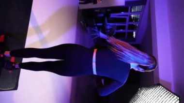 İki sporcu kız stüdyoda neon ışıkta spor yapıyor.