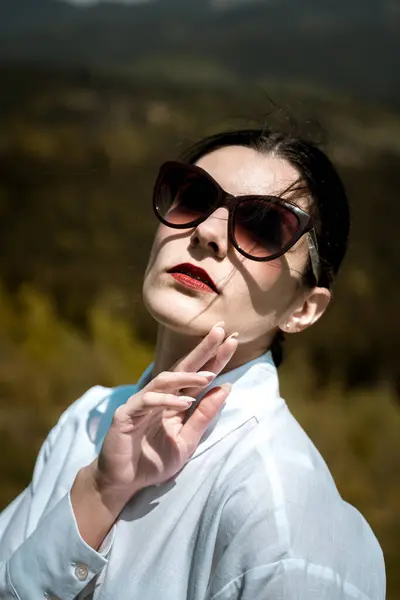 stock image Stylish woman in a white shirt and glasses posing against the backdrop of mountains