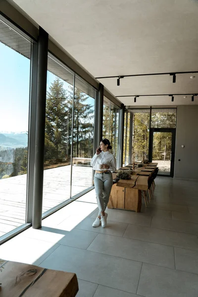 stock image Pretty woman in a white shirt and glasses posing against the backdrop of a modern mountain hotel.Businessman woman concept