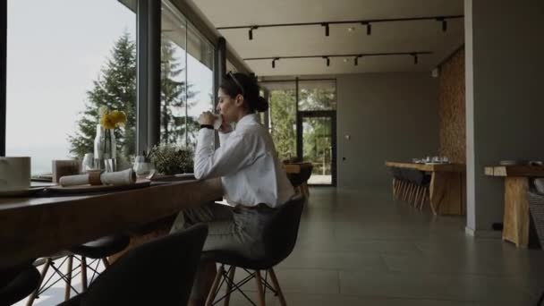 一个漂亮的女人在餐馆里喝咖啡 从窗户到喀尔巴阡山 欣赏着令人难以置信的美景 — 图库视频影像