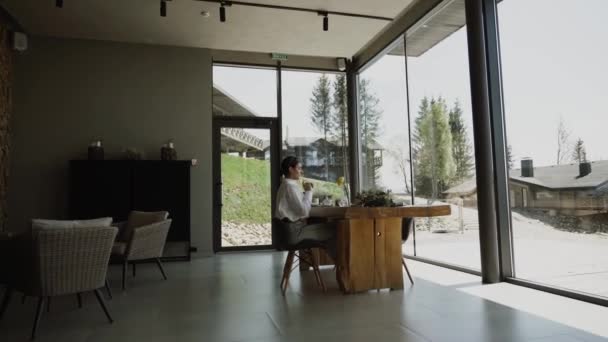 一个漂亮的女人在餐馆里喝咖啡 从窗户到喀尔巴阡山 欣赏着令人难以置信的美景 — 图库视频影像