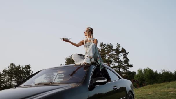 Стильная Женщина Очках Запускает Дрон Закате Сидя Крыше Автомобиля Концепция — стоковое видео