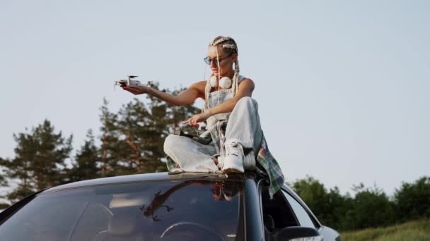 Стильна Жінка Окулярах Запускає Безпілотник Заході Сонця Сидячи Даху Автомобіля — стокове відео