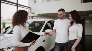 Otomobil satış merkezinde. Araba satıcısı genç bir aileye yeni otomobil satıyor. Araba galerisinde yeni bir araba seçen genç ve güzel bir çift.