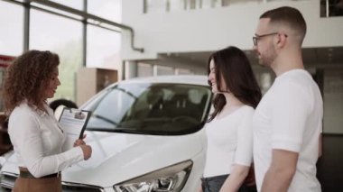 Otomobil satış merkezinde. Araba satıcısı genç bir aileye yeni otomobil satıyor. Araba galerisinde yeni bir araba seçen genç ve güzel bir çift.
