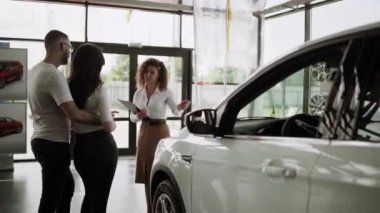 Otomobil satış merkezinde. Araba satıcısı genç bir aileye yeni otomobil satıyor. Araba galerisinde yeni bir araba seçen genç ve güzel bir çift.