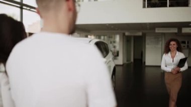 Otomobil satış merkezinde. Araba satıcısı genç bir aileye yeni otomobil satıyor. Araba galerisinde yeni bir araba seçen genç ve güzel bir çift.