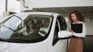 Otomobil satış merkezinde. Araba satıcısı genç bir aileye yeni otomobil satıyor. Araba galerisinde yeni bir araba seçen genç ve güzel bir çift.