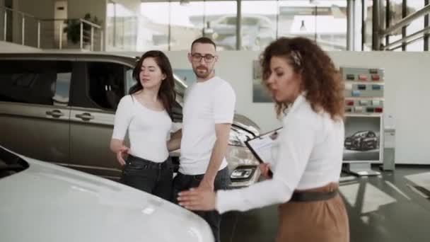 在汽车销售中心 汽车销售人员把新车卖给年轻的家庭 漂亮的年轻夫妇在汽车展示室挑选新车 — 图库视频影像