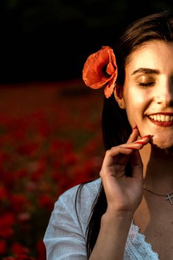 Haşhaş tarlasında poz veren güzel bir kadın. Beyaz elbiseli bir kadın çiçeklerin arasında duruyor. Genç kız gülümsüyor. Mutluluk kavramı. Haşhaş çiçekleriyle dolu bir çayırda dinlen.