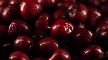  Siyah arka planda dönen, su damlacıklarıyla kaplı kırmızı kirazlar. Islak kirazlar siyah bir uçakta dönüyor.