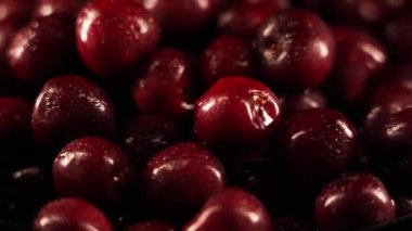 Su damlacıklarıyla kaplı kırmızı kirazlar, ıslak siyah bir zemin üzerinde dönüyorlar.