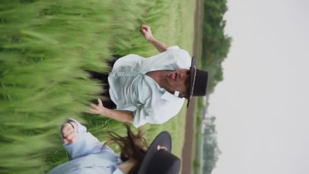 帽子をかぶった3人の若いダンサーのチームが緑の小麦畑で踊って楽しんでいます 垂直ビデオ — ストック動画