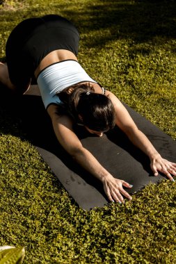 Formda, spor elbiseli güzel bir kadın evinin yanındaki yeşil çimlerin üzerinde lotus pozisyonunda otururken meditasyon yapıyor. Evde yoga egzersizi yapan genç bir kadın. 