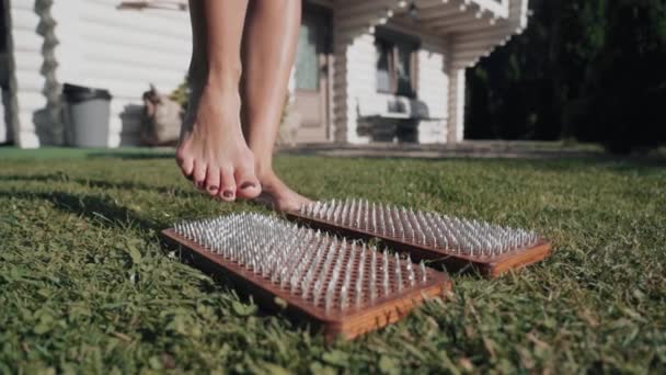 女人站在木制瑜伽板上 用钉子做练习和冥想 替代药物穴位压力 恢复能力 站在木制木板上 草坪上钉有钉子 — 图库视频影像