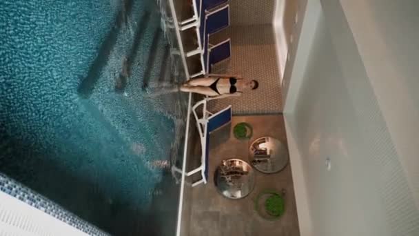 若い幸せなカップルは 山の豪華なウェルネスセンターで屋内プールで楽しんでリラックスします 垂直ビデオ — ストック動画