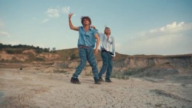 İki erkek dansçı günbatımında çölde modern dans eder.