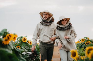Genç arıcılar arılarla çalışır ve bal yerler. Genç bir arı yetiştiricisi ailesi ayçiçekli bir tarlada bal toplar. Bal toplama konsepti