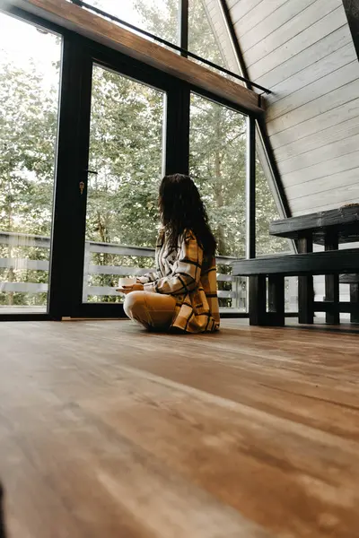 A woman rests and meditates in a house in the forest in autumn. Retreat and meditation concept