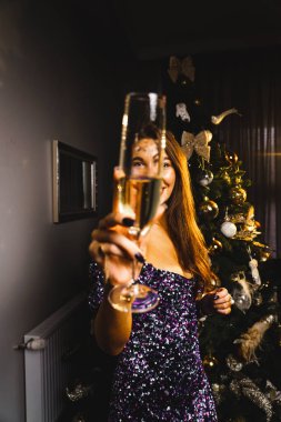 Bir bardak şampanyayla, parlak mavi bir elbisenin yanında parlak bir Noel ağacının yanında beyaz bir kadının portresi. Yeni yıl ve Noel konsepti.
