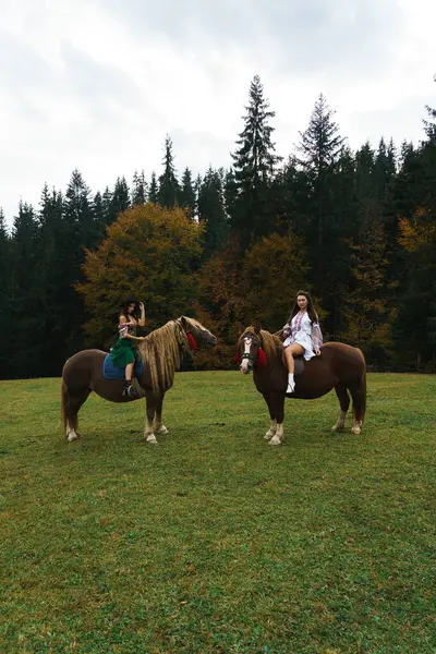 Genç kadınlar ulusal Ukrayna elbiseleriyle Karpat dağlarında atlara biniyorlar. Dağlarda atlarla fotoğraf çekimi. Ukrayna kültür kavramı