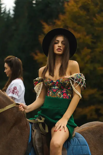 Genç kadınlar ulusal Ukrayna elbiseleriyle Karpat dağlarında atlara biniyorlar. Dağlarda atlarla fotoğraf çekimi. Ukrayna kültür kavramı