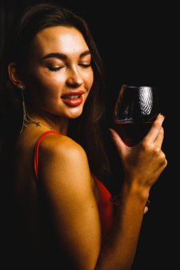 Kırmızı elbiseli seksi bir kadının ellerinde bir kadeh kırmızı şarap.