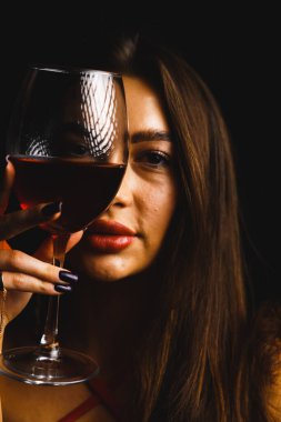 Kırmızı elbiseli seksi bir kadının ellerinde bir kadeh kırmızı şarap.
