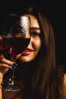 Kırmızı elbiseli seksi bir kadının ellerinde bir kadeh kırmızı şarap.