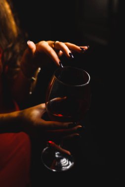 Kırmızı elbiseli seksi bir kadının ellerinde bir kadeh kırmızı şarap.