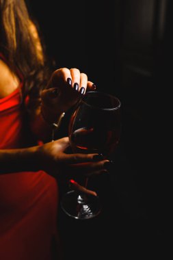 Kırmızı elbiseli seksi bir kadının ellerinde bir kadeh kırmızı şarap.