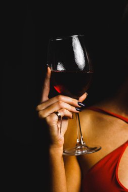 Kırmızı elbiseli seksi bir kadının ellerinde bir kadeh kırmızı şarap.