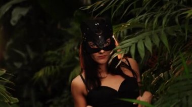 Palmiye ağaçlarının arasında tropik bir bahçede poz veren BDSM kedi maskeli seksi kadın. BDSM kavramı 44k