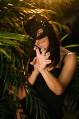 Palmiye ağaçlarının arasında tropik bir bahçede poz veren BDSM kedi maskeli seksi kadın. BDSM konsepti.
