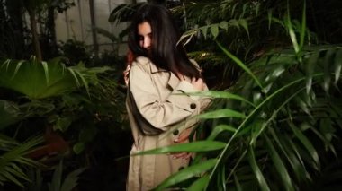 Tropik bir bahçede poz veren siyah elbiseli seksi bir kadın. Moda fotoğrafçılığı kavramı. 4k