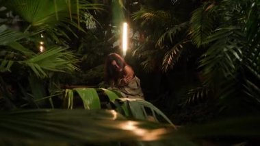 Tropik bir bahçede poz veren siyah elbiseli seksi bir kadın. Moda fotoğrafçılığı kavramı. 4k