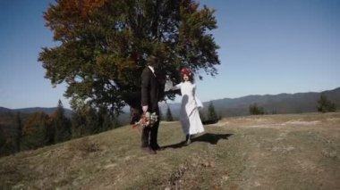 Otantik düğün çifti sonbaharda gün batımında dağlarda yürüyor. Düğün konsepti dağlarda. Sinema sahnesi 4K.