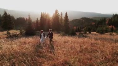 Otantik düğün çifti sonbaharda gün batımında dağlarda yürüyor. Düğün konsepti dağlarda. Sinema sahnesi 4K.