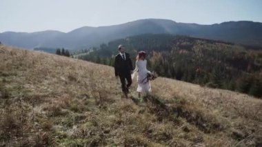 Otantik düğün çifti sonbaharda gün batımında dağlarda yürüyor. Düğün konsepti dağlarda. Sinema sahnesi 4K.