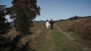 Otantik düğün çifti sonbaharda gün batımında dağlarda yürüyor. Düğün konsepti dağlarda. Sinema sahnesi 4K.