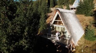 Birbirine aşık bir çift dağlardaki bir İskandinav evinin terasında poz veriyor. Düğün konsepti. 4k