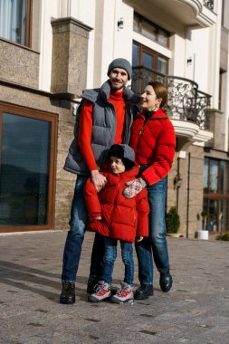 Genç aile babası anne ve oğlu otelin yakınında kırmızı kışlık giysiler içinde poz veriyorlar. Mutlu aile kavramı