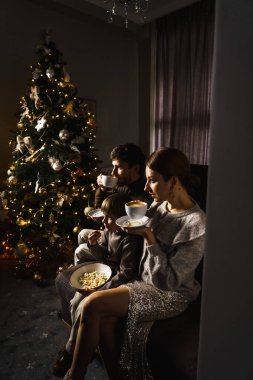 Mutlu aile Noel 'i kutlar, film izler ve yılbaşı ağacının yanında patlamış mısır ve pizza yer. Dikey fotoğraf