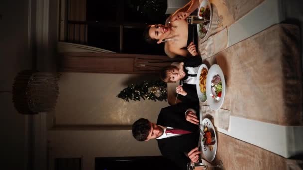 メリークリスマス 幸せな家族が家で夕食を食べています お祝いの休日と木の近くのトータルネス クリスマステーブルで父 母と息子 クリスマスと新年のコンセプト 垂直ビデオ — ストック動画
